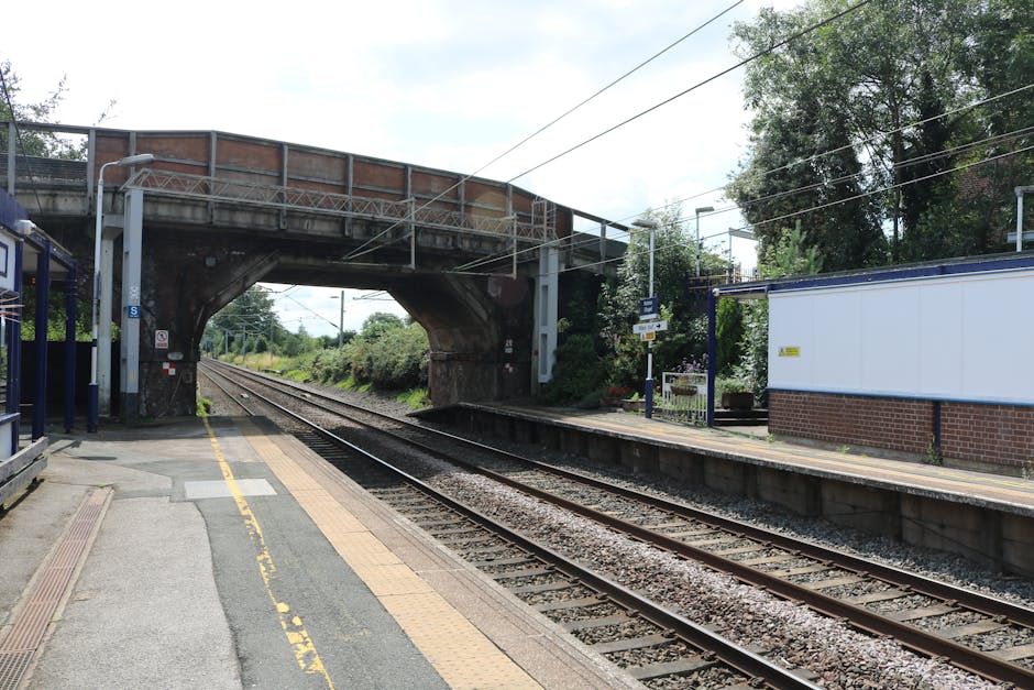 A view of Upminster train station platform with parallel railway tracks extending into the distance, bordered by a concrete edge and a yellow safety line. The platform surface is composed of grey pavi