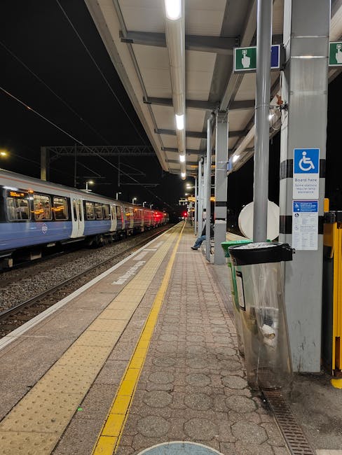 A view of Upminster train station platform with parallel railway tracks extending into the distance, bordered by a concrete edge and a yellow safety line. The platform surface is composed of grey pavi